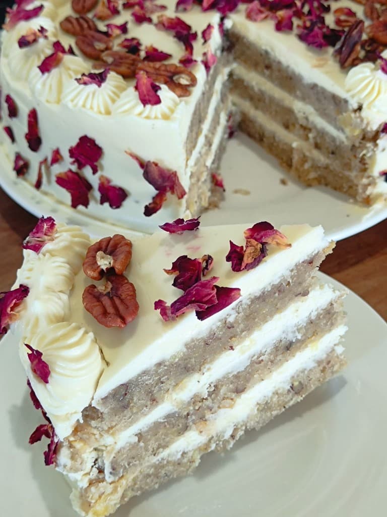 Three-layer cake with white frosting, pecans, and rose petals